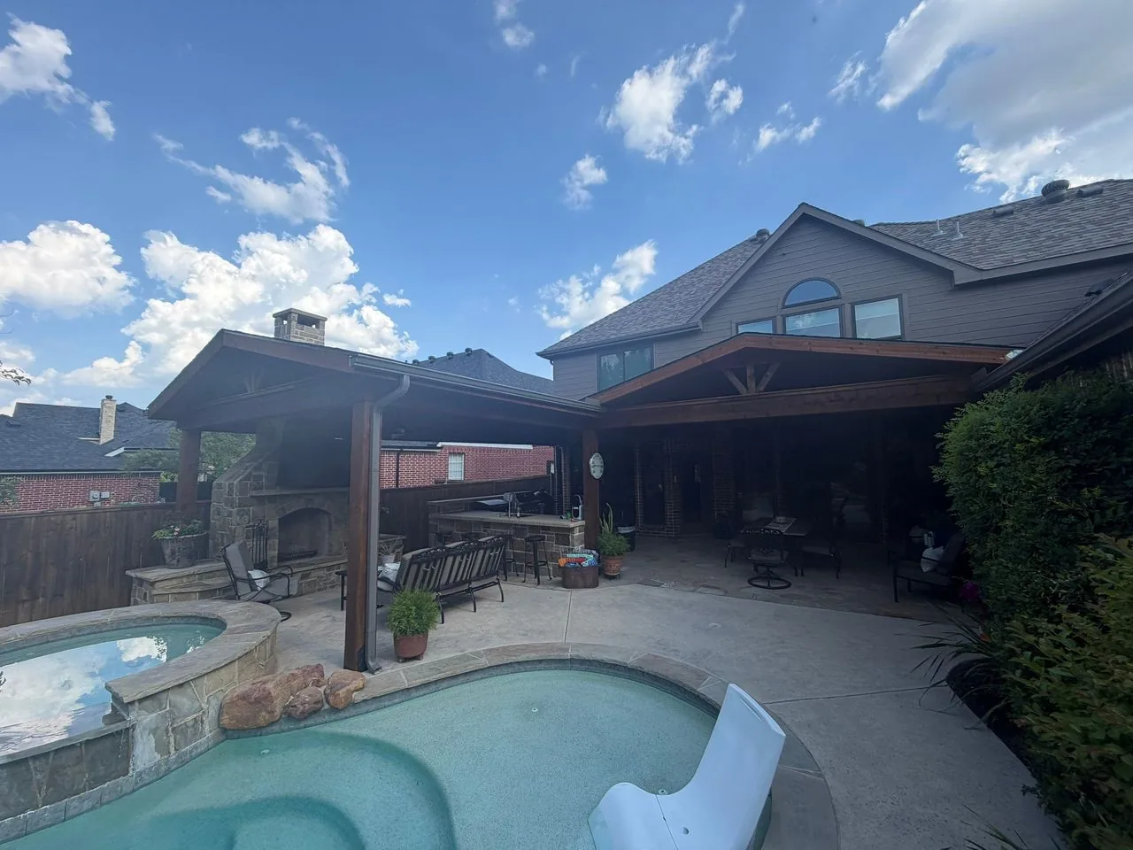 Finished dual-gable covered patio with outdoor kitchen and stone fireplace beside the pool