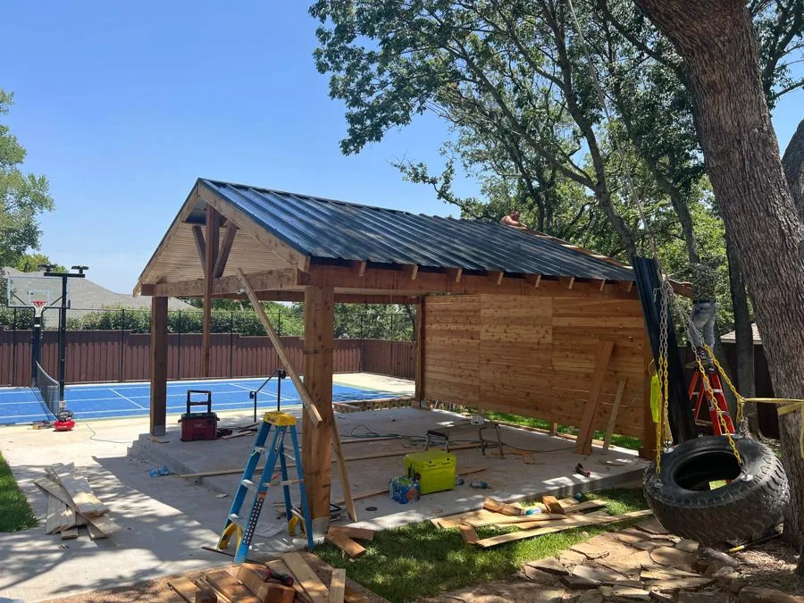 Large freestanding cedar pavilion with a metal roof beside a sport court